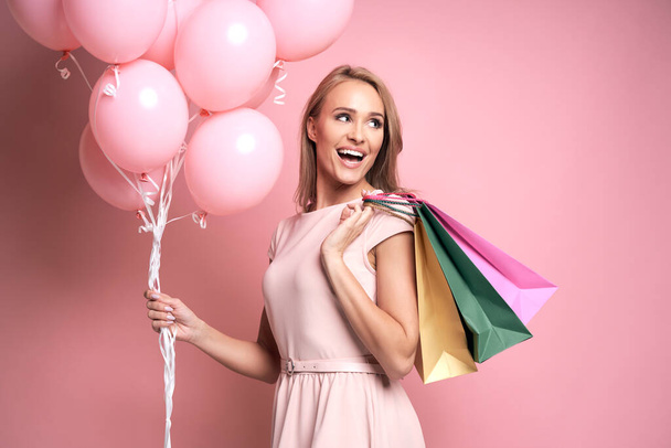Studioaufnahme einer kaukasischen jungen Frau mit Einkaufstüten und rosa Luftballons - Foto, Bild