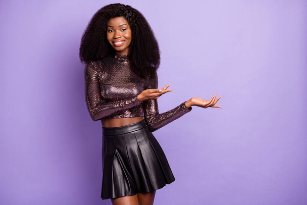 Photo of cheerful african girl hands demonstrate empty space wear glossy shirt isolated purple color background - Foto, afbeelding