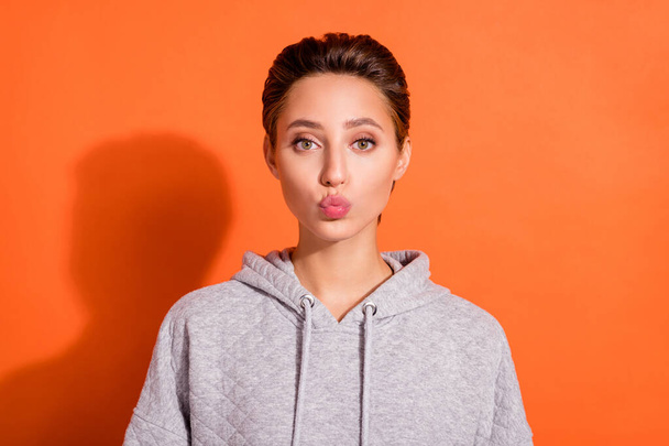 Photo of sweet charming young woman dressed grey hoodie sending you kiss isolated orange color background - Zdjęcie, obraz