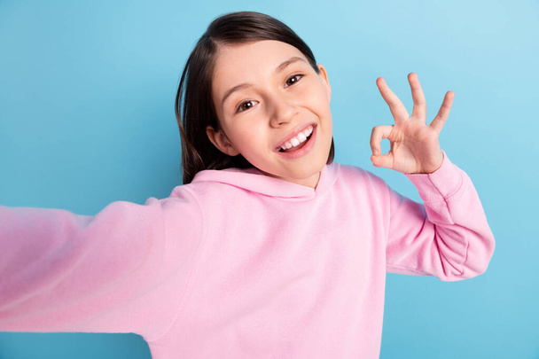 Photo of optimstic long hair girl do selfie show okey wear pink sweatshirt isolated on blue background - Foto, immagini