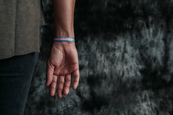 closeup of a young person, seen from behind, wearing a wristband patterned with a transgender pride flag on a gray background with some blank space on the right - Фото, зображення