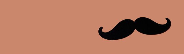 a black moustache on a brown background with some blank space on the left, in a panoramic format to use as web banner or header - Photo, Image