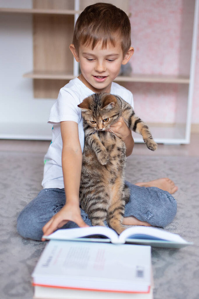 Um menino bonito a ler um livro com um gato. Escola em casa. Ensino à distância. Férias. Quarentena durante a pandemia do Coronavirus. Bloqueio - Foto, Imagem