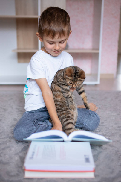 Kedisiyle kitap okuyan sevimli küçük bir çocuk. Evde eğitim. Mesafe öğrenme. Tatillerde. Coronavirüs salgını sırasında karantina. Kilitlenme - Fotoğraf, Görsel