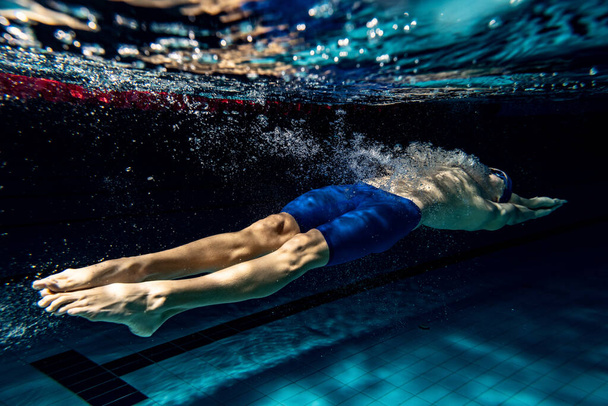 Underwater shooting. One male swimmer training at pool, indoors. Underwater view of swimming movements details. - Fotoğraf, Görsel
