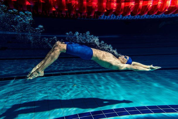 Underwater shooting. One male swimmer training at pool, indoors. Underwater view of swimming movements details. - Fotó, kép