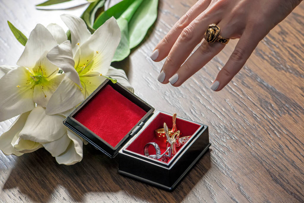 Bir kadının eli, üzerinde beyaz çiçekler olan bir mücevher kutusuna uzanır. Arka planda güzel romantik bir arka plan - Fotoğraf, Görsel