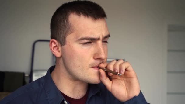 ένας άντρας ξεφυσάει πάνω στο τσιγάρο στέκεται μπροστά από το παράθυρο - Πλάνα, βίντεο