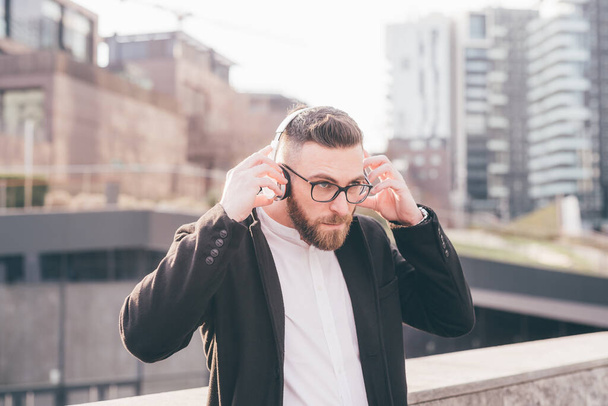 Fiatal jóképű szakállas férfi szabadban hallgat zenét vezeték nélküli fejhallgató hallgatás streaming zene - Fotó, kép