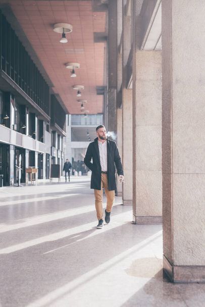 Молодий бородатий білий елегантний бізнесмен розслабляє ходити на відкритому повітрі курити сигарети
 - Фото, зображення