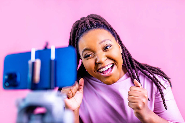 hispanic woman with cool dreadlocks pigtails wear pink dress in studio chatting with her subscribers by phone camera - Photo, image