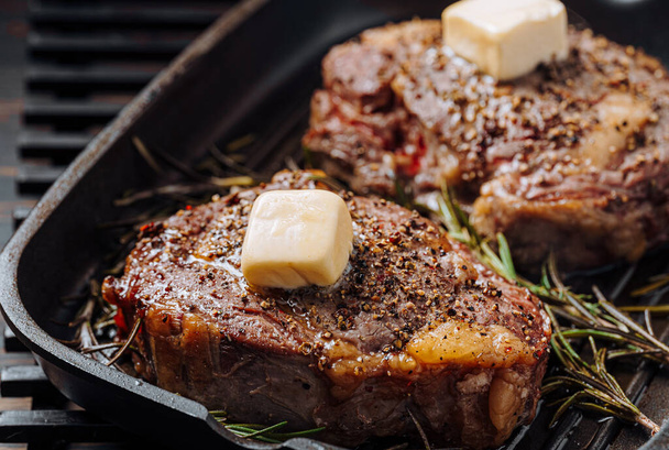 cooking sumptuous steaks in a grill pan with butter spreading over the steak seasoned with ground pepper and salt with rosemary sprigs - Foto, afbeelding