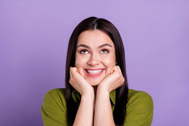 Photo of dreamy shiny young woman wear khaki outfit arms cheeks looking up empty space smiling isolated violet color background - Foto, imagen