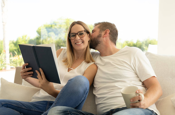 Spending nice time at home. Beautiful young loving couple bonding to each other and smiling while woman holding a book - Photo, Image