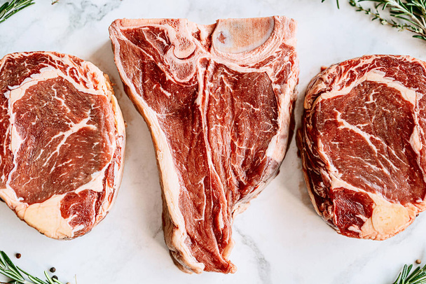 three delicious steaks ready to grill on a white marble surface - Фото, изображение
