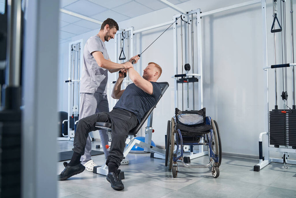 Hombre con discapacidad tira de la correa de estiramiento con la ayuda del terapeuta - Foto, imagen