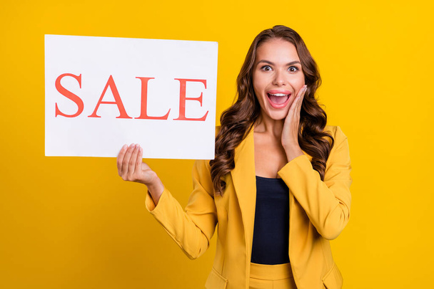 Photo of attractive excited young lady wear suit jacket holding sale card hand arms cheek cheekbone isolated yellow color background. - Foto, Imagen