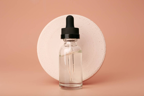 Still life with skin serum in dark bottle with round gypsum circle on dark beige background. Concept of anti aging or anti acne skin care and beauty treatment  - Fotografie, Obrázek