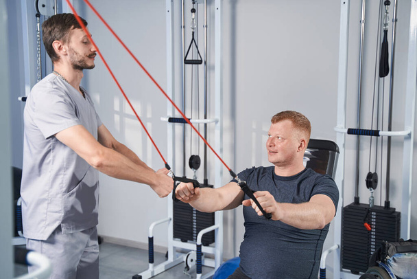 Doctor help cerebral palsy man do exercises with stretching simulator - Zdjęcie, obraz