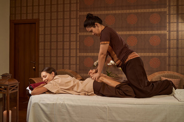 Masseuse utilizing leg stretching technique on her client - Foto, afbeelding