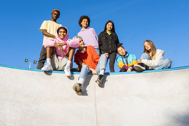 Πολυπολιτισμική ομάδα νεαρών φίλων που δένουν σε εξωτερικούς χώρους και διασκεδάζουν - Κομψά δροσερά εφηβικά πάρτι στο πάρκο για πατινάζ - Φωτογραφία, εικόνα