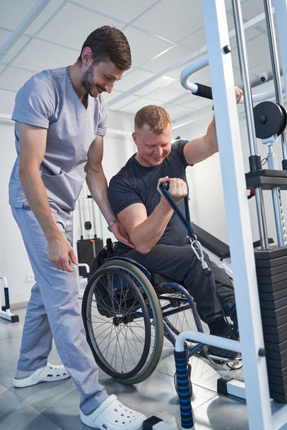 ハッピーセラピストは車椅子の患者を治療する。スポーツ傷害の男 - 写真・画像