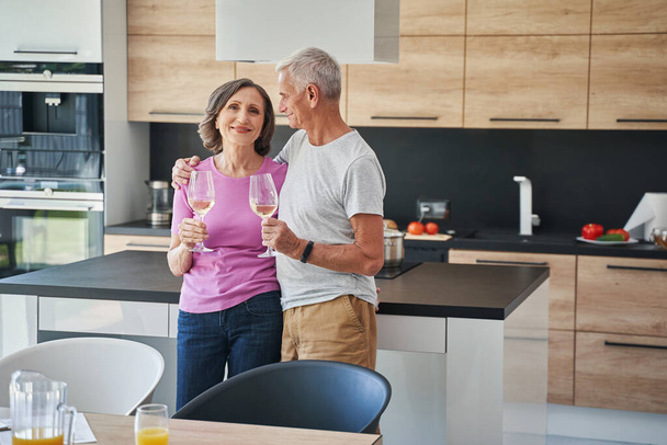Celebrating senior couple drinking champagne in kitchen - Фото, изображение