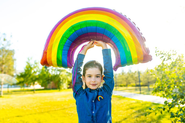 cute little brunette girl holding an air colorful rainbow balloon in summer park - Photo, Image