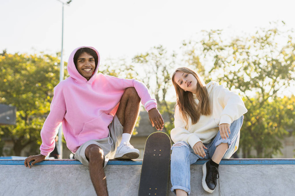 Multicultural group of young friends bonding outdoors and having fun - Stylish cool teens gathering at urban skate park - 写真・画像