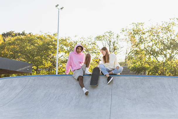 Multicultural group of young friends bonding outdoors and having fun - Stylish cool teens gathering at urban skate park - Photo, image