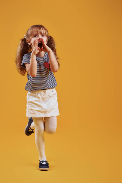 Cute little girl in casual clothes have fun in the studio against yellow background. - Foto, immagini