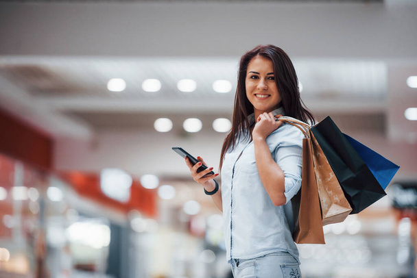 Брюнетка женщина в супермаркете со многими пакетами и телефон в руках имеют торговый день. - Фото, изображение