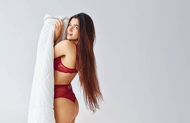 Woman in red underwear covering her body by towel in the studio against white background. - Foto, afbeelding