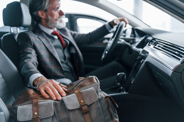 Fashionable senior man with grey hair and mustache on vacation with bag inside modern automobile. - Fotoğraf, Görsel