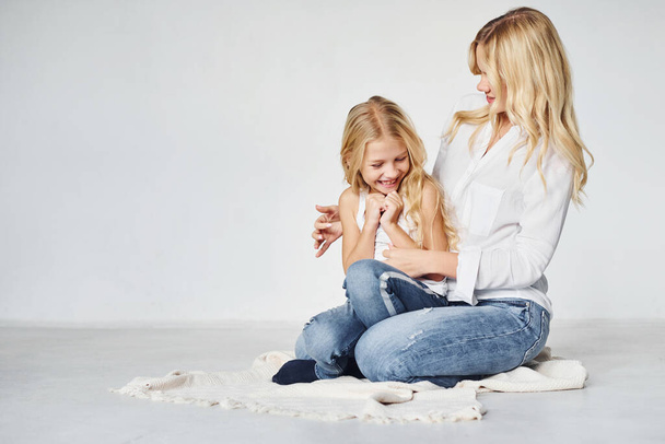 Mother with her daughter together is on the ground in the studio with white background. - Foto, afbeelding