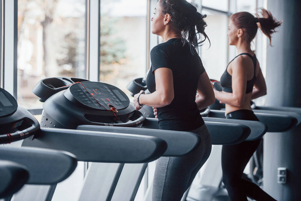 Two young girls in sportive clothes is in the gym together at treadmill. - Valokuva, kuva