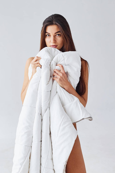 Woman covering her body by towel in the studio against white background. - Foto, imagen