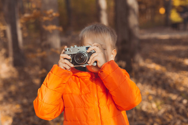 Retro kameralı çocuk sonbahar doğasında dışarıda fotoğraf çekiyor. Boş zaman ve fotoğrafçı konsepti - Fotoğraf, Görsel