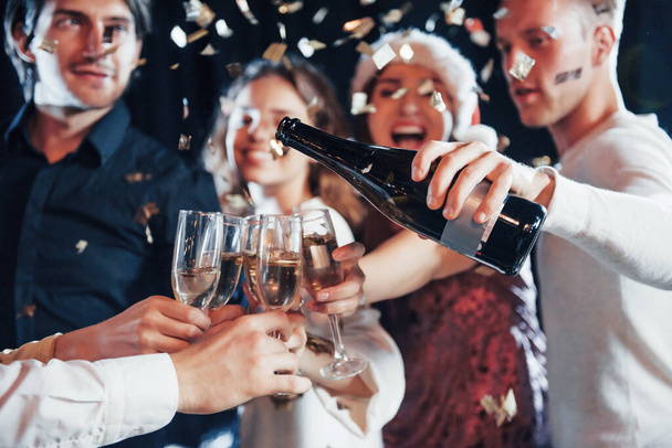 Pouring champagne. Group of cheerful friends celebrating new year indoors with drinks in hands. - Foto, immagini