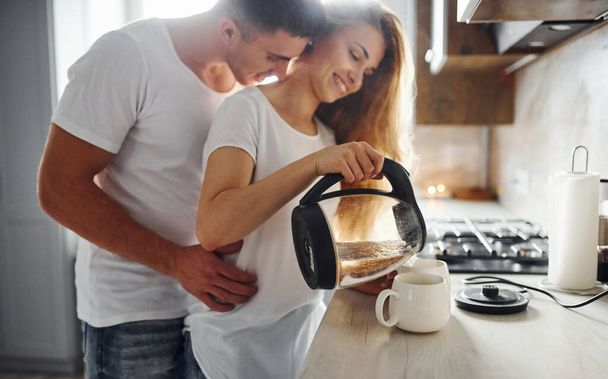 Young couple at morning together standing on the modern kitchen. - Фото, изображение