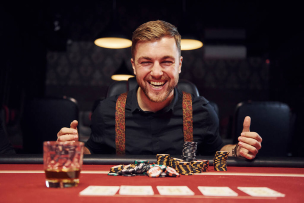Happy elegant young man sits in casino and celebrate his victory in poker game. - Foto, Bild