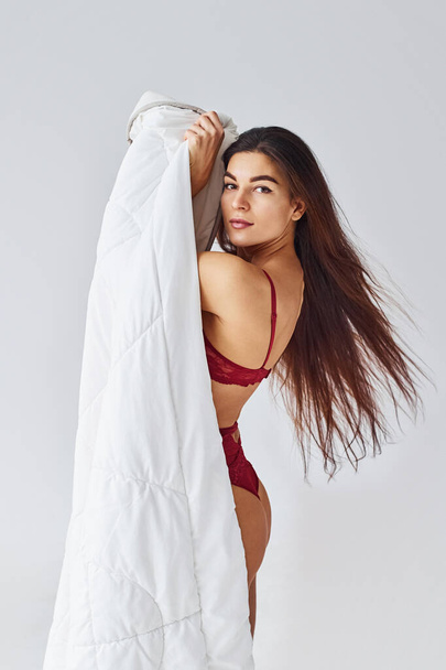 Woman in red underwear covering her body by towel in the studio against white background. - Valokuva, kuva