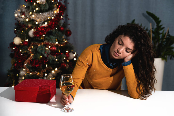 Young newly divorced woman sitting alone at home feeling depressed and lost without a husband and is celebrating Christmas and New Year holidays alone with alcohol.   - Foto, afbeelding