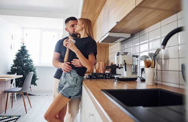 With cup of fresh drink. Morning for young married couple that standing indoors in the kitchen. - Fotografie, Obrázek