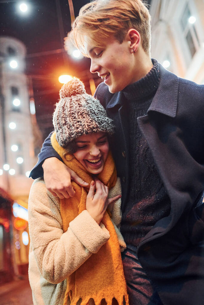 Positive young couple in warm clothes embracing each other on christmas decorated street. - Foto, immagini