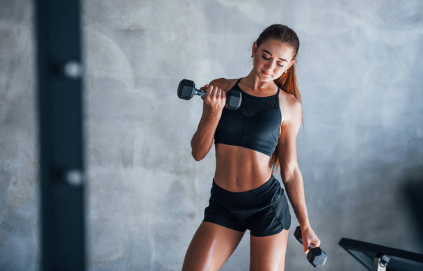 Young fitness woman is in the gym with dumbbells in hands. - Photo, Image