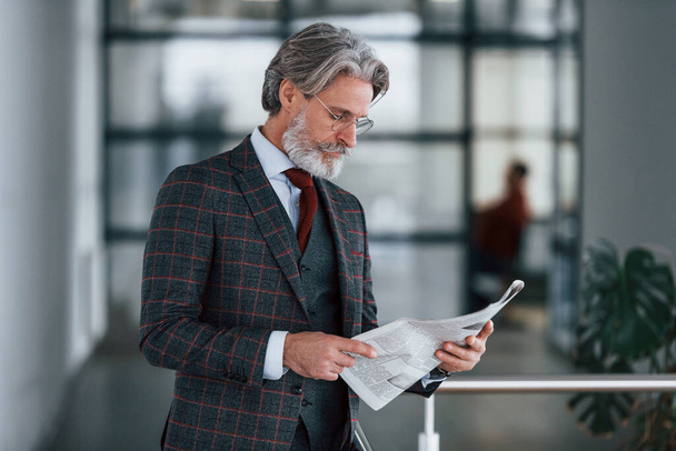 Senior-Geschäftsmann in Anzug und Krawatte mit grauen Haaren und Bart hält Zeitung in den Händen. - Foto, Bild