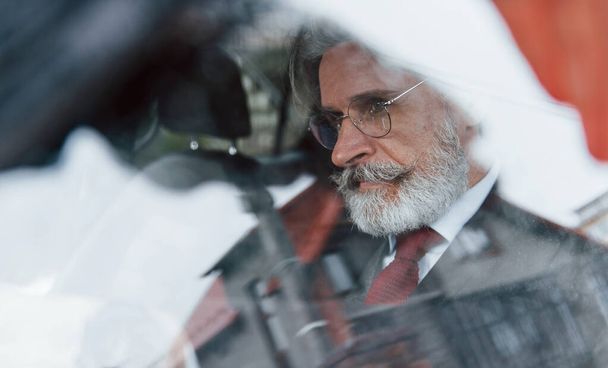 View through the glass of stylish senior man with grey hair and mustache that is in the modern car. - Photo, Image