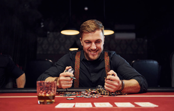 Happy elegant young man sits in casino and celebrate his victory in poker game. - Foto, Imagem