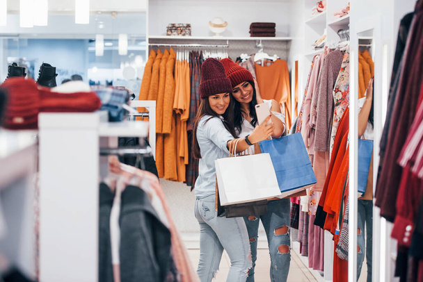 Looking for a warm clothes. Two young women have a shopping day together in the supermarket. - Zdjęcie, obraz
